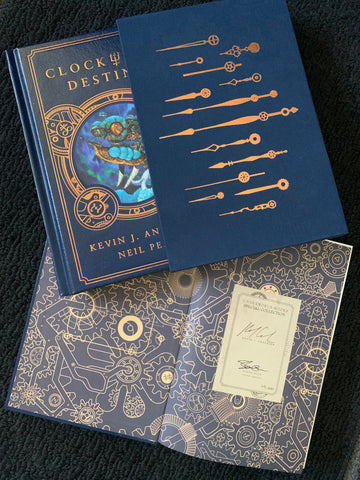 Photo: Clockwork Destiny by Kevin J. Anderson and Neil Peart. Two copies shown, one in a blue slipcase matching the blue faux leather of the book cover. The second book is open to the front endsheet which has a signed bookplate on it with signatures from Kevin J. Anderson and Steve Otis.